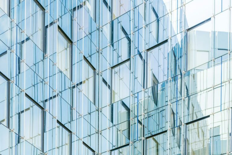 Reflective blue glass facade with repeating structural boundaries, used as an editorial metaphor for AI controls.